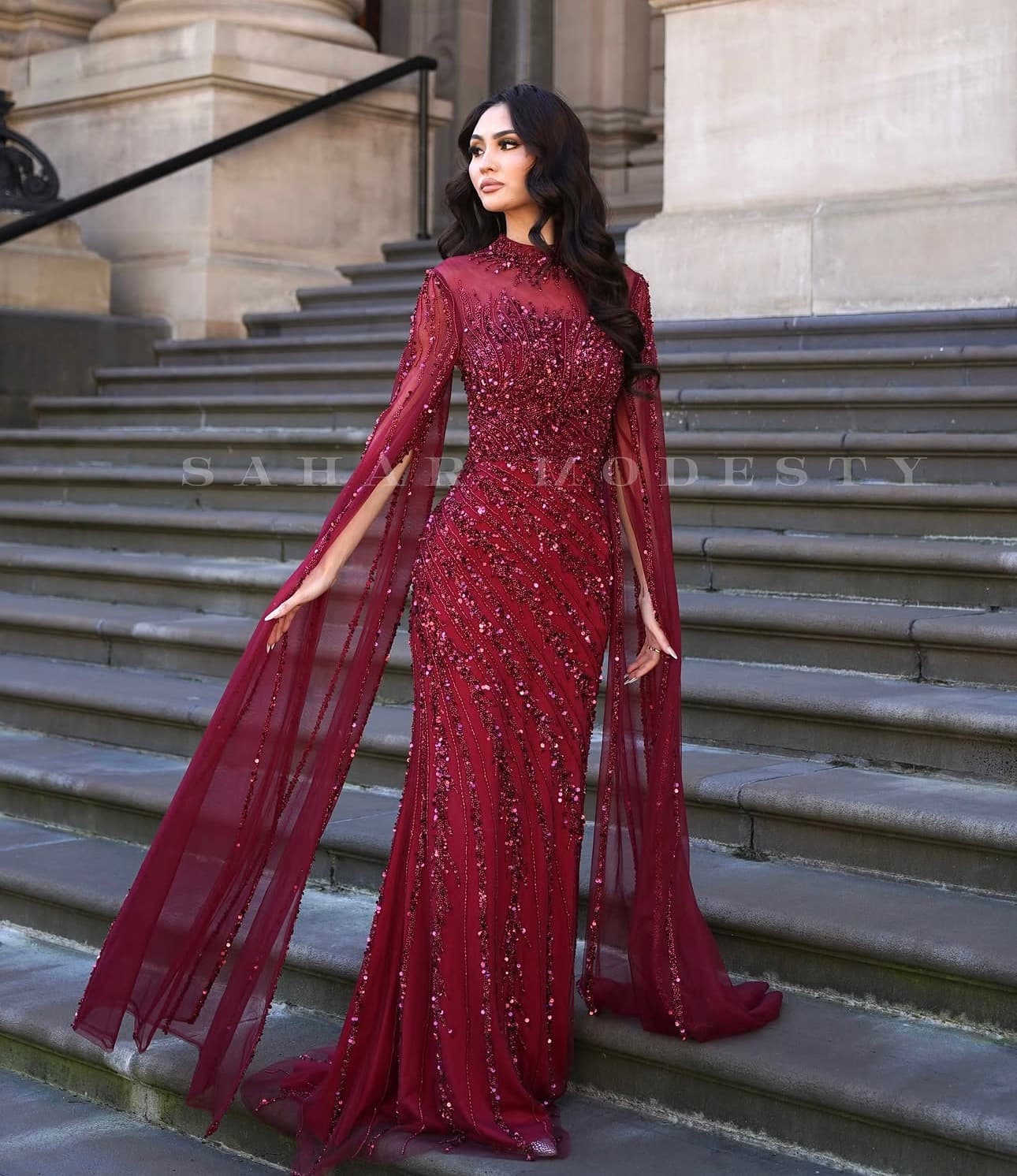 Burgundy beaded modest cape sleeve gown on stone steps.