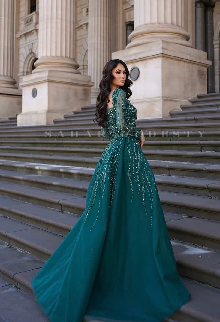 Back view of a model in an emerald beaded modest ballgown with a covered back.