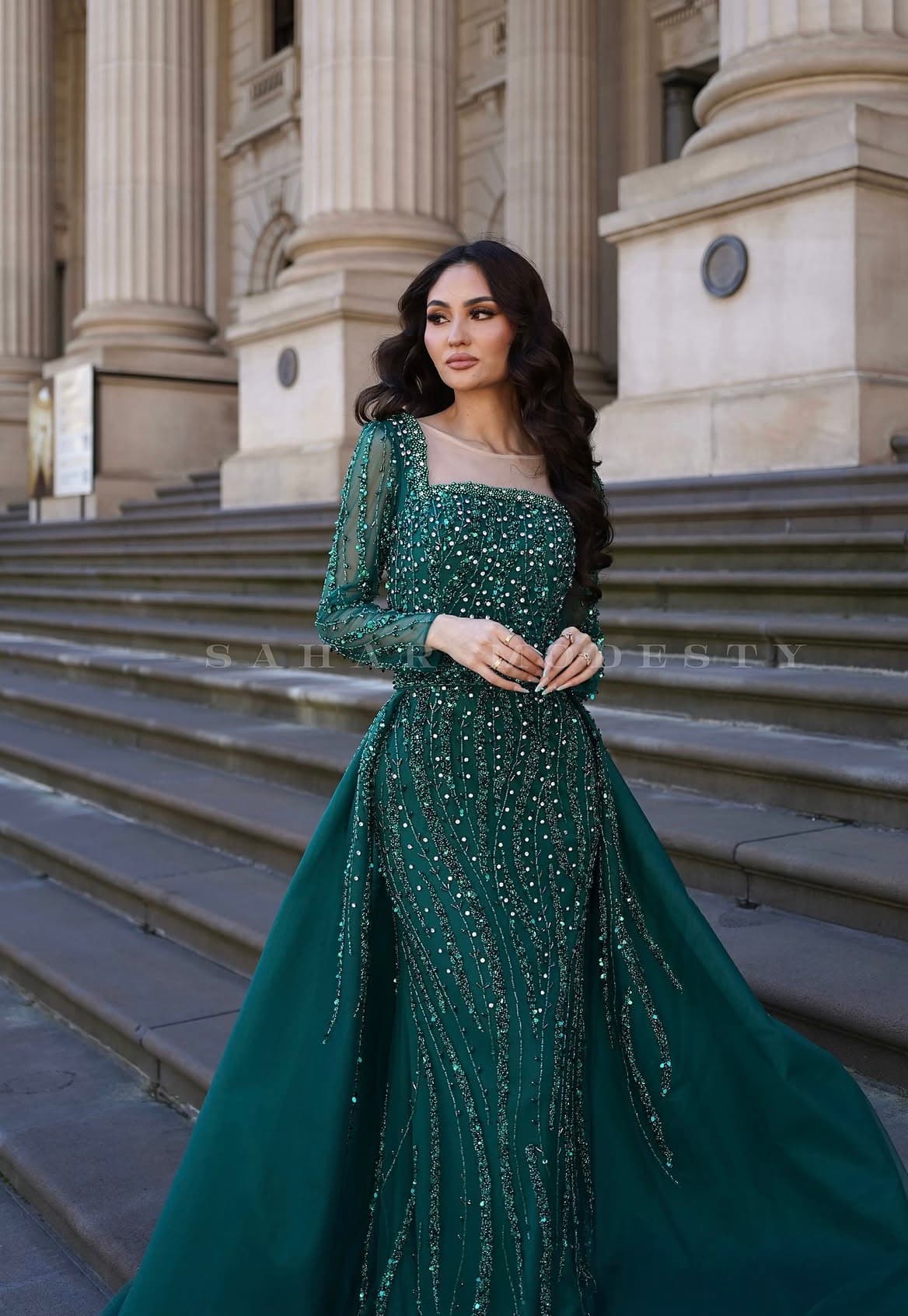 Model in an emerald beaded modest court gown with long sleeves and a full skirt.